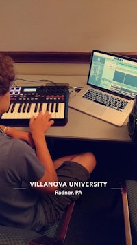 a boy sitting at a desk with a laptop and a keyboard