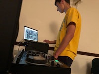 a young man in a yellow shirt standing next to a dj mixer